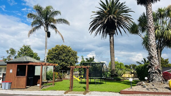 A residential area with a small wooden structure, a playground, and several palm trees.
