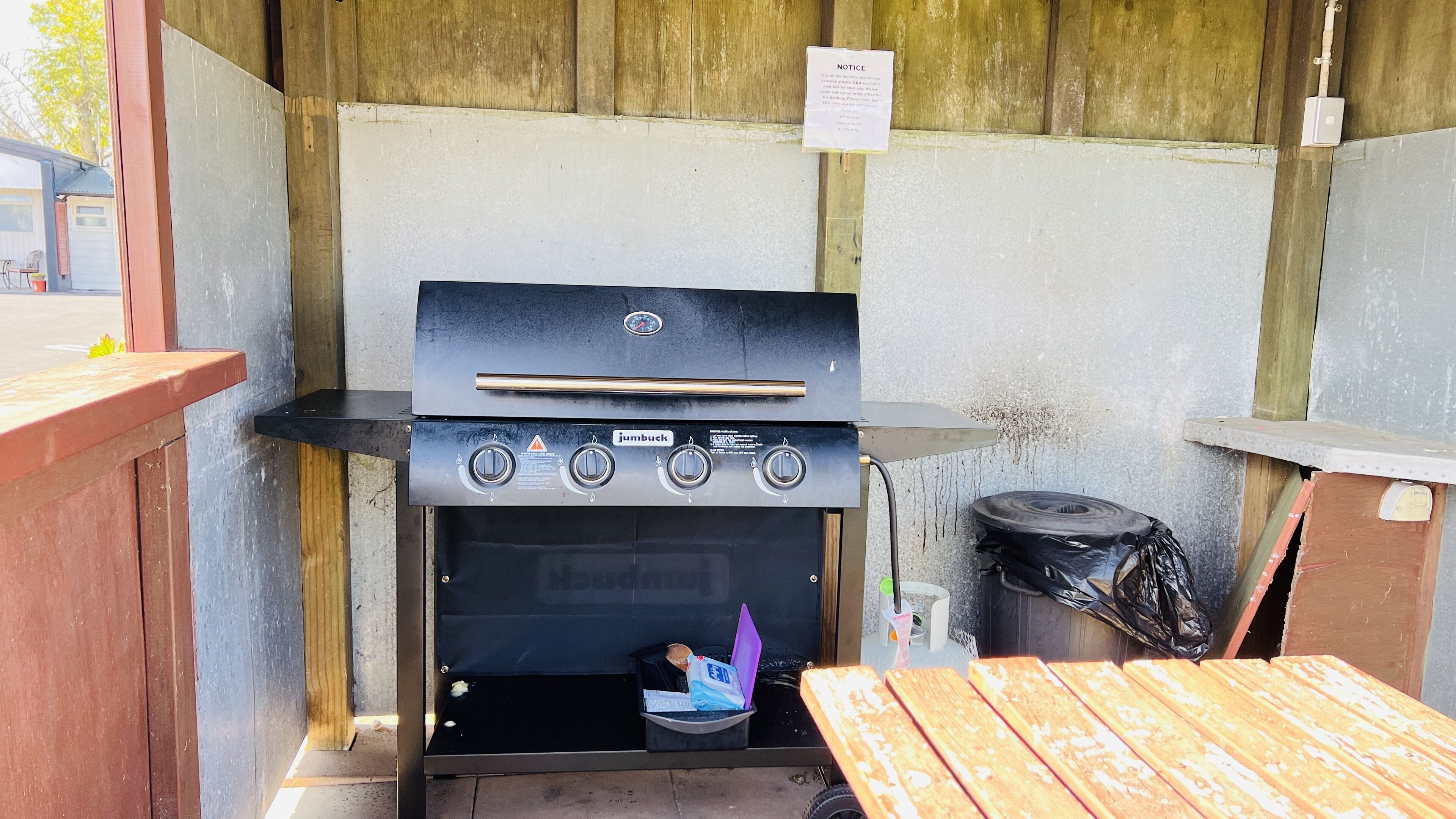 A Jumbuck outdoor grill with a wooden table and a trash bin nearby.
