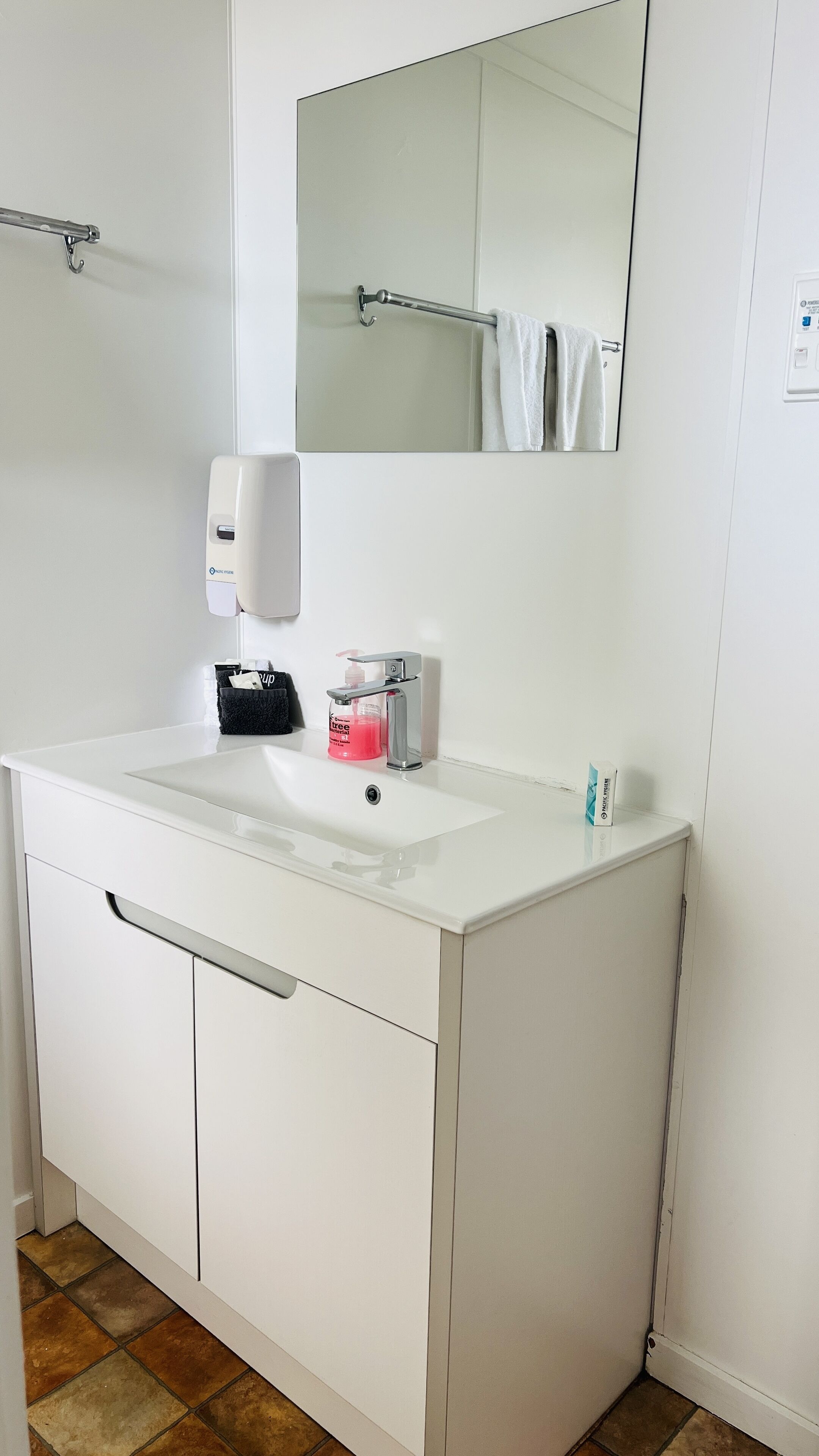 Un bagno moderno con un lavandino bianco, uno specchio, un porta asciugamani, un erogatore di sapone e una bottiglia di sapone per le mani.