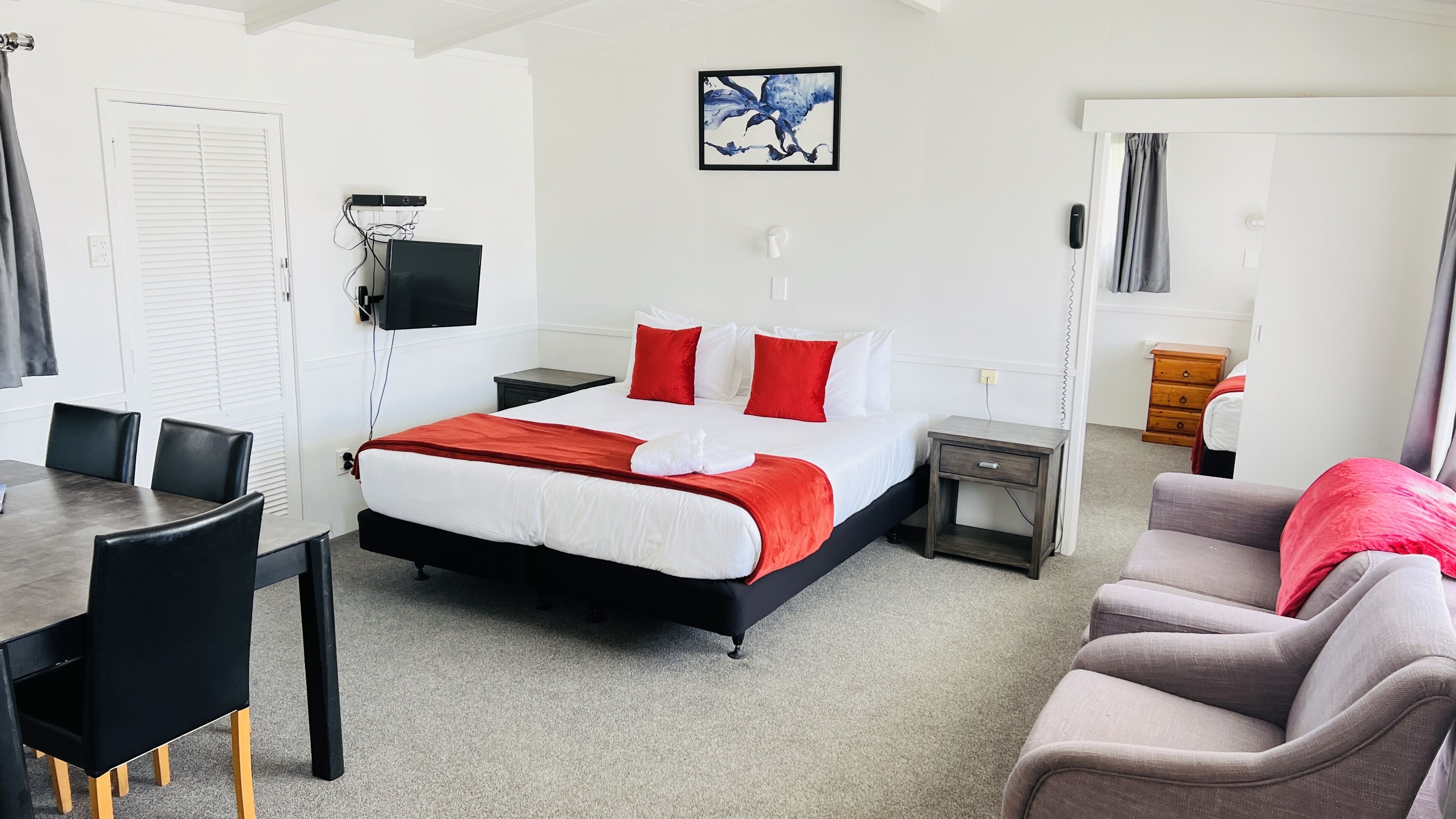 A hotel room with a bed, a desk, a chair, a TV, and a painting on the wall.
