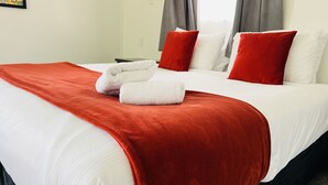 Una habitación de hotel con una cama bien hecha, almohadas rojas y blancas, y una colcha roja.
