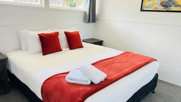 Een net opgemaakt bed met witte en rode beddengoed, een grijze nachtkastje en een raam met gordijnen.