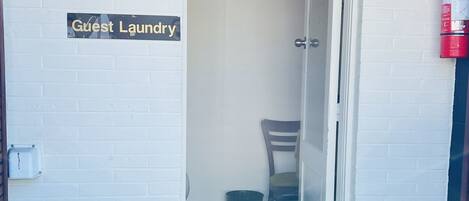 A guest laundry area with a sign, a chair, and a fire extinguisher.