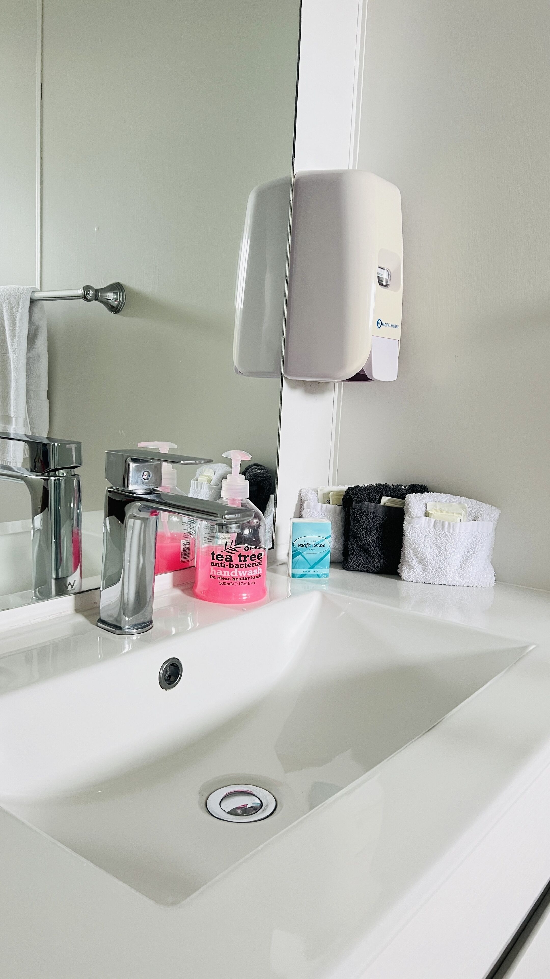 A bathroom sink with a mirror, a soap dispenser, and various toiletries.