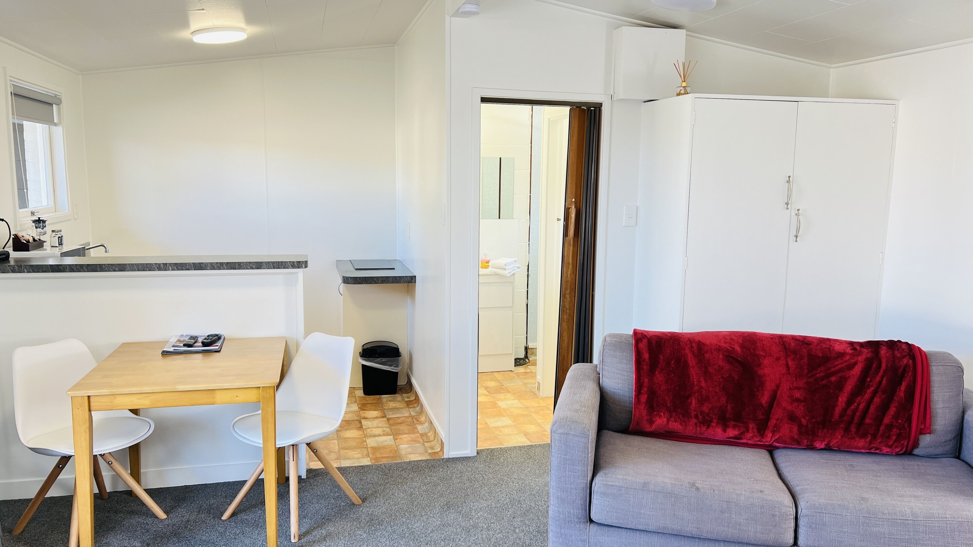 A compact living space with a kitchenette, a dining area, and a seating area with a red blanket.