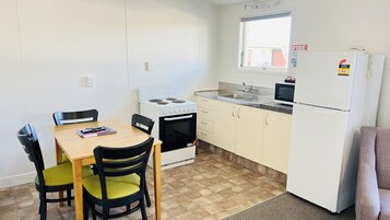 A compact kitchen with a stove, microwave, and refrigerator. There is a dining table with chairs and a window above the sink.
