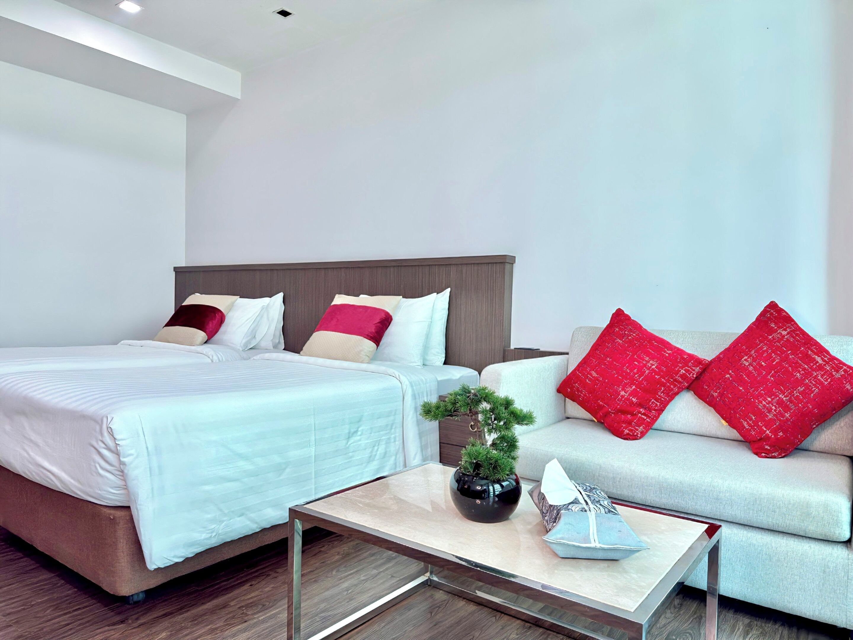A modern hotel room with a large bed, a sofa, a small table, and a potted plant.
