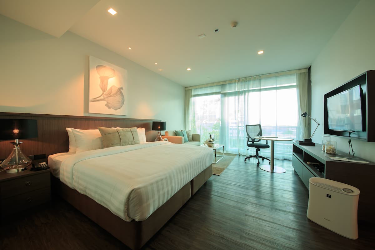 Een hotelkamer met een groot bed, nachtkastje, lamp en een televisie aan de muur.