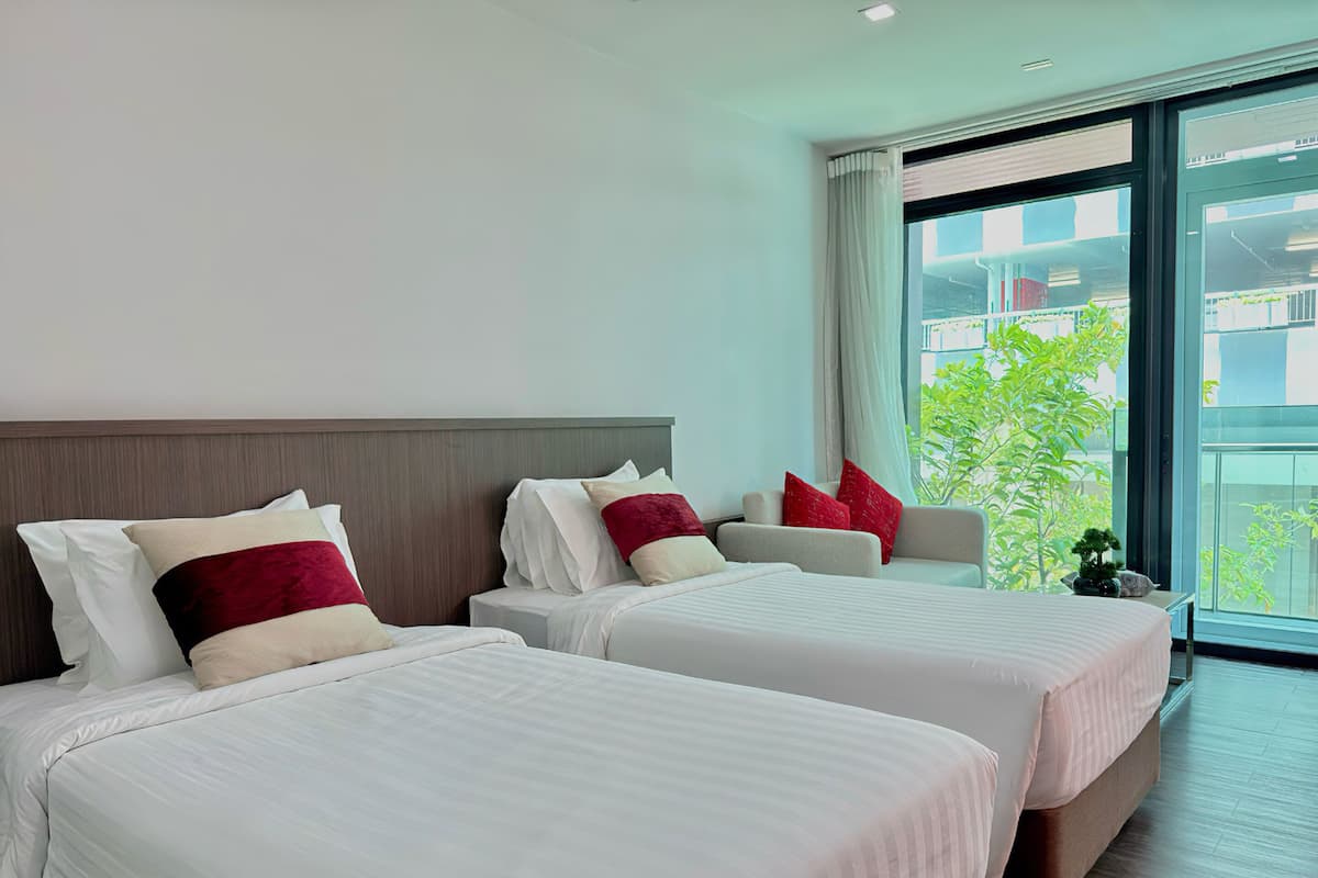 Een hotelkamer met twee bedden, een groot raam en uitzicht op groen.