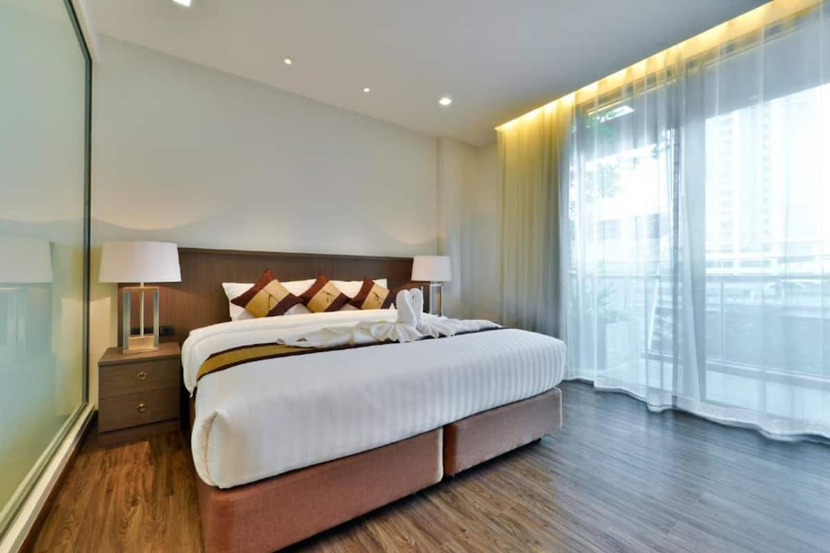 Een moderne hotelkamer met een groot bed, houten vloeren en een groot raam met transparante gordijnen.