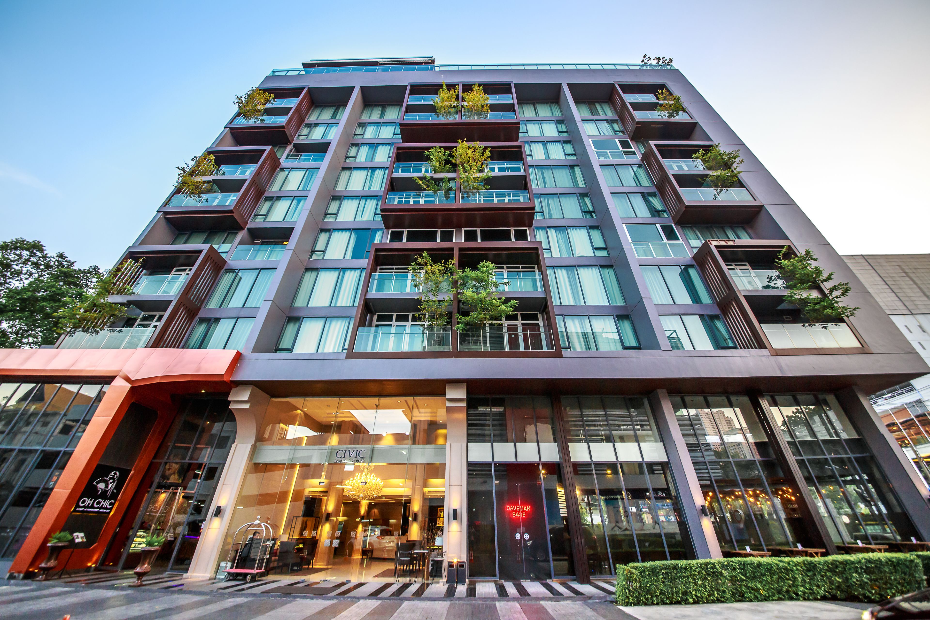 Un hôtel moderne à plusieurs étages, doté de grandes fenêtres et d’espaces ext érieurs aménagés pour se détendre.