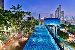 Une piscine à débordement située sur le toit, offrant une vue panoramique sur la ville, et entourée d’arbres et de bâtiments modernes.
