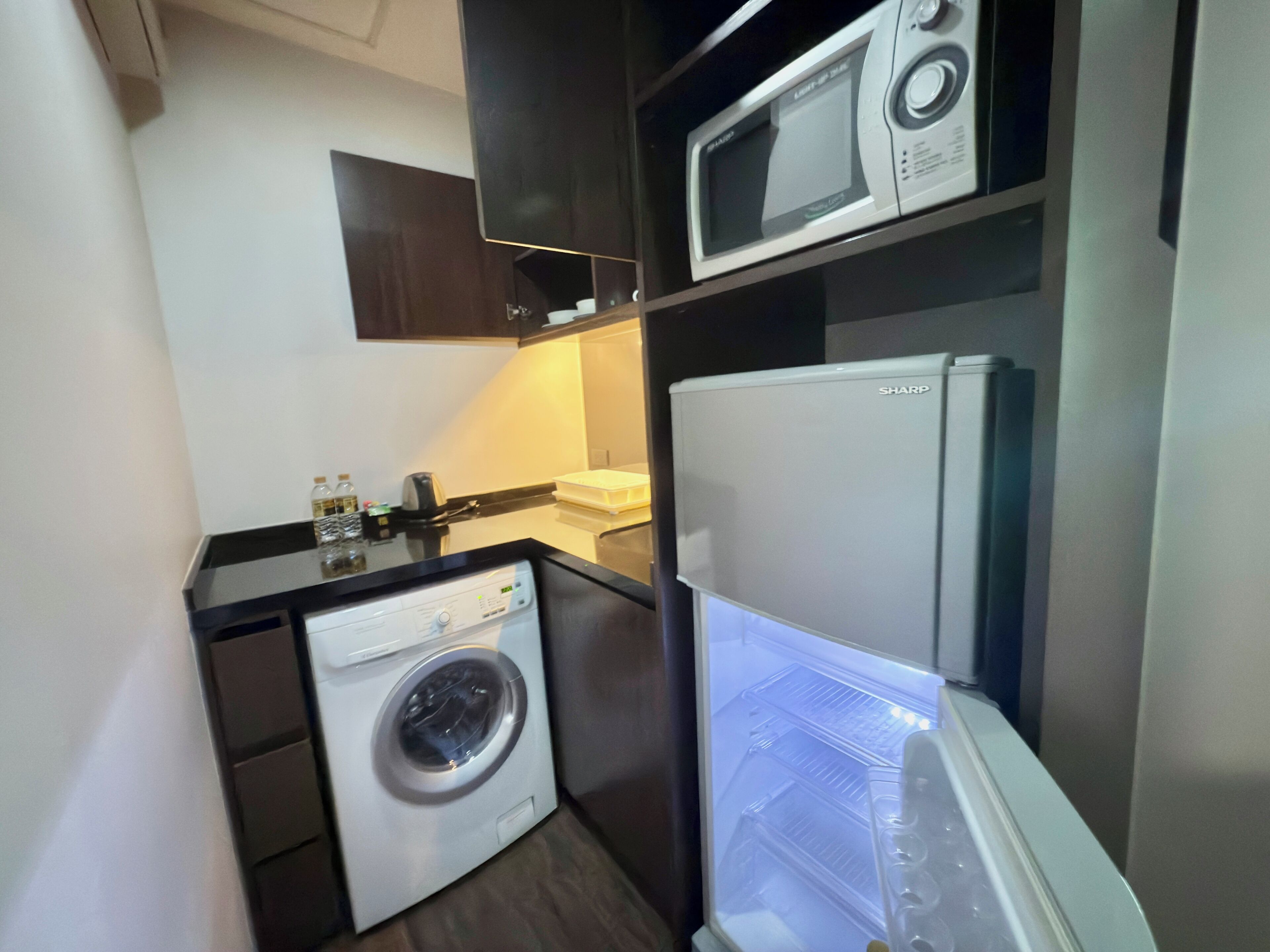 A compact kitchenette with a washing machine, a microwave, and a refrigerator.