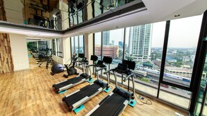 A gym with treadmills, exercise bikes, and weights, large windows with a city view.