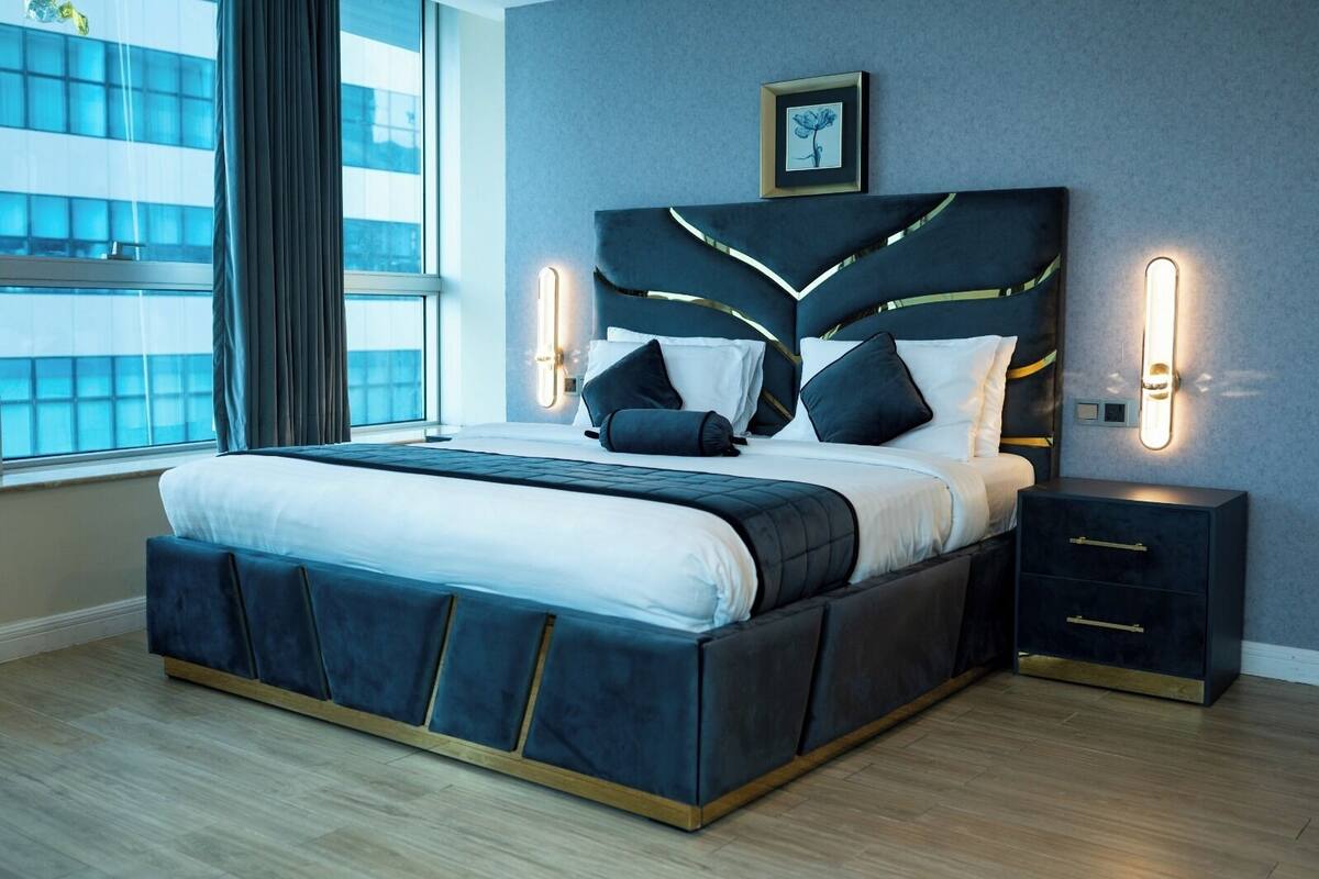 Un dormitorio moderno con una cama grande, mesitas de noche y vistas a un edificio a través de la ventana.