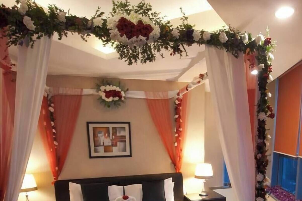 Un dormitorio con cama, dos mesitas de noche, un cuadro colgado en la pared y una cama con dosel decorada con motivos florales.