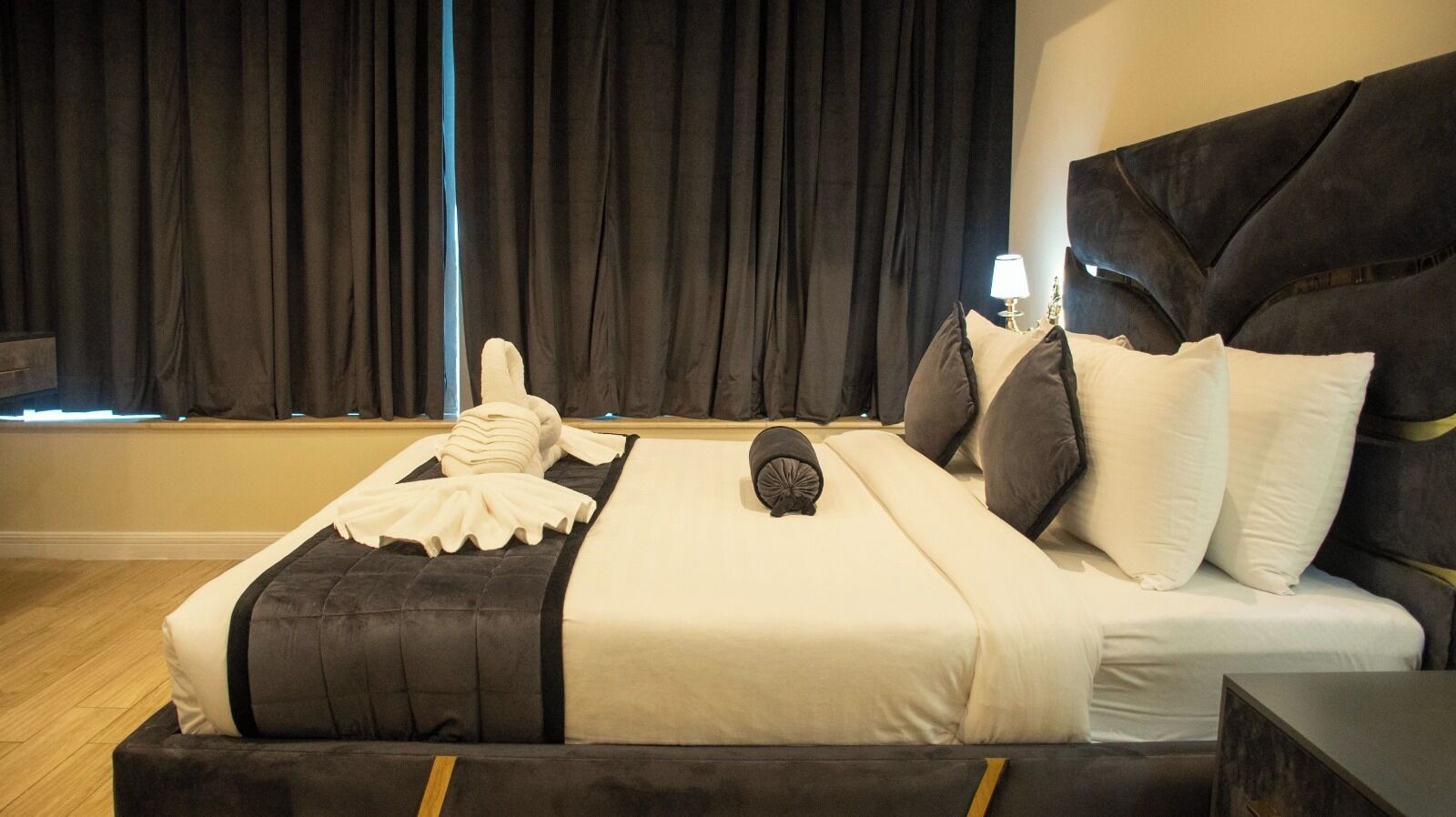 Una cama con cabecera oscura, ropa de cama blanca y una toalla al lado.