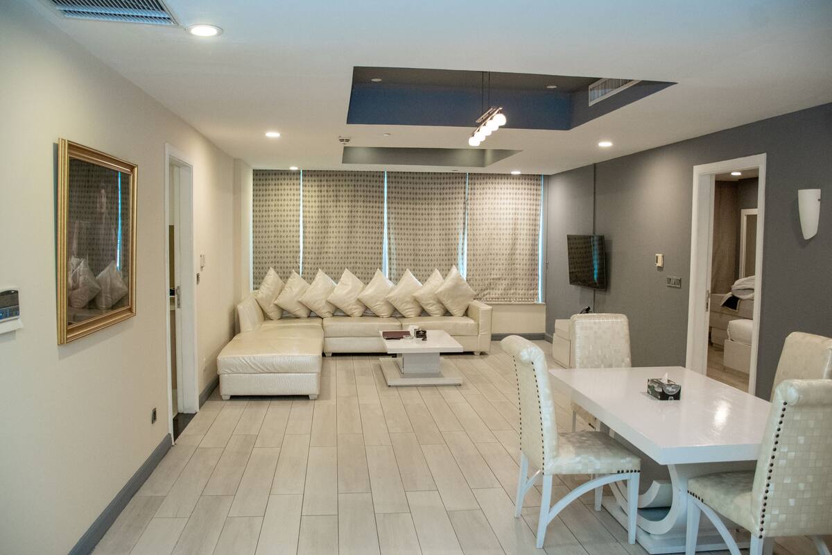 Una sala de estar moderna con un sofá seccional, una mesa de comedor y un televisor montado en la pared.