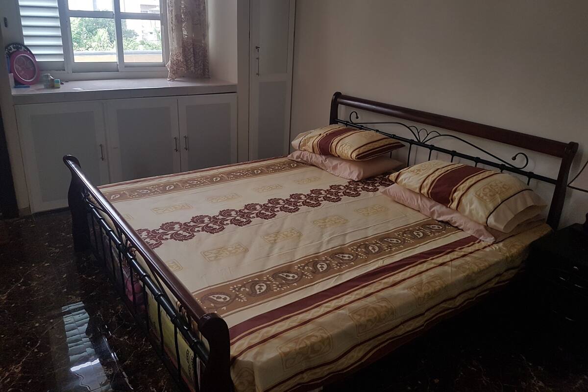 Une chambre à coucher avec un lit, une fenêtre avec des rideaux, une armoire et un radiateur.