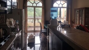 Une cuisine équipée d’un réfrigérateur, d’un four à micro-ondes et d’une cuisinière. On y trouve deux fenêtres avec des rideaux, un distributeur d’eau et une bouteille de soda sur le comptoir.