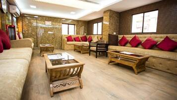A spacious lobby with a beige sofa set, wooden coffee tables, and red cushions.