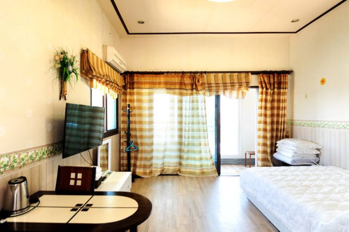 A hotel room with a bed, a desk with a chair, a television, and a window with curtains.