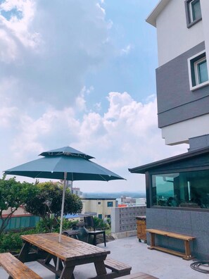 An outdoor patio area with a wooden table and a green umbrella, overlooking a cityscape.