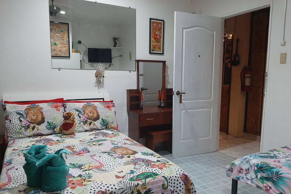 A bedroom with a bed, a chair, a desk, and a door leading to another room.