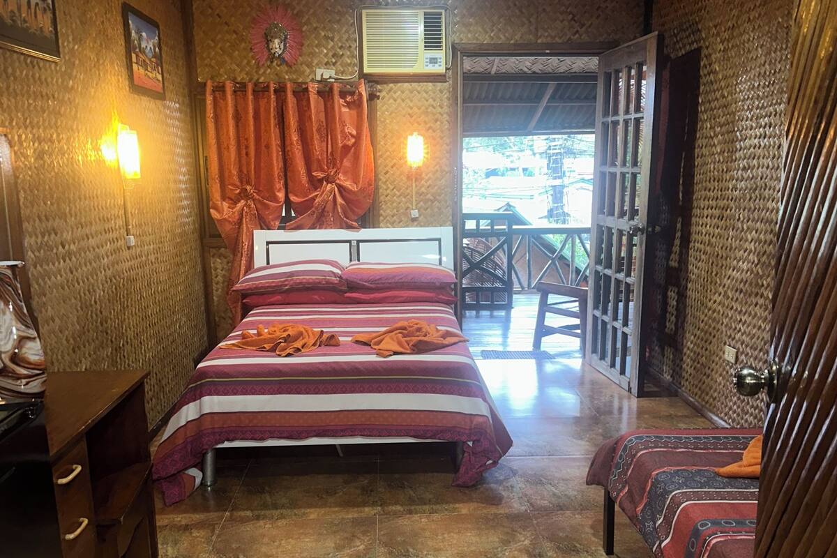 A bedroom with a bed, a desk, a ceiling fan, and a view of the outside.