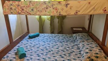 A single bed with a peacock feather pattern, a green towel, and a floral blanket.