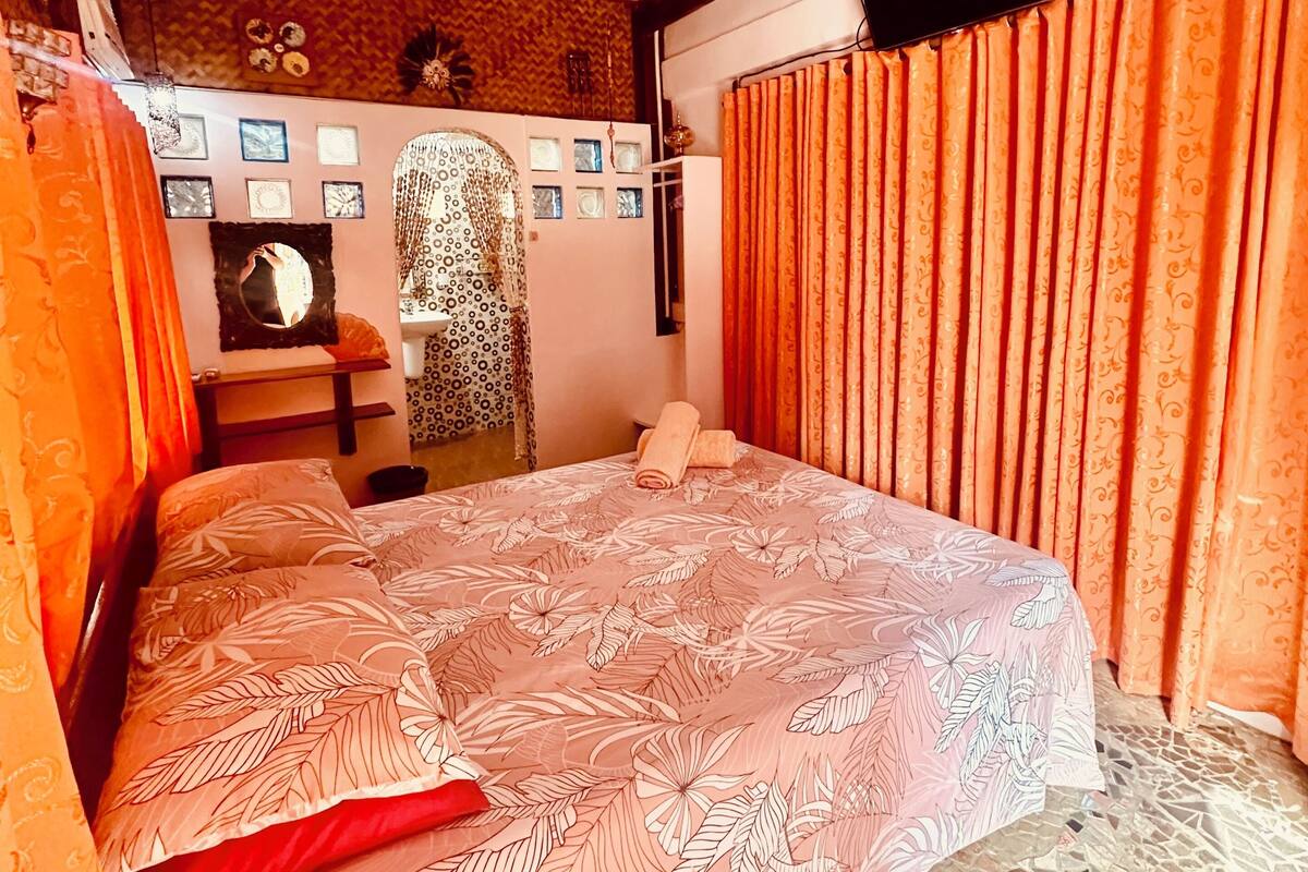 A room with a bed, a ceiling fan, a television, and patterned curtains.