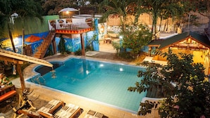 A swimming pool with a wooden deck and lounge chairs, surrounded by tropical plants and a mural. - Lala Panzi (Puerto Princesa)