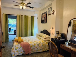 Ein Schlafzimmer mit einem Bett, einem Schreibtisch, einem Stuhl, einem Deckenventilator und einer Tür, die auf einen Balkon führt.