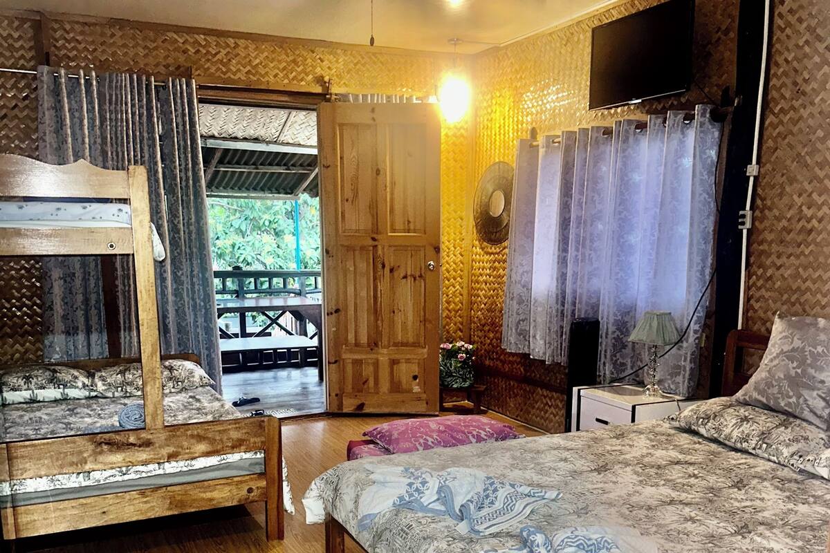 A room with a bunk bed, a single bed, a ceiling fan, a TV, and a wooden floor.