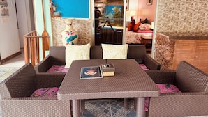 A wicker lounge area with a table and cushions, a decorative vase, and a view into a room with a bed and a painting. - Lala Panzi (Puerto Princesa)