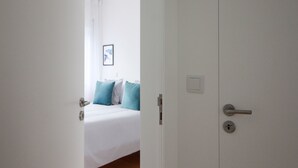 A hotel room with a bed, a door, and a light switch on the wall.