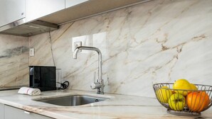 A modern kitchen with a marble countertop, a stainless steel sink, and a fruit bowl.