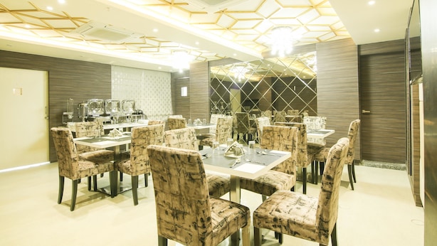 A dining area with hexagonal ceiling design, marble-patterned chairs, and a buffet setup. - Treebo Hoops - Airport, VIP Road (Barasat)
