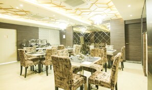 A dining area with hexagonal ceiling design, marble-patterned chairs, and a buffet setup. - Treebo Hoops - Airport, VIP Road (Barasat)
