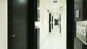 A modern hotel corridor with black doors, white walls, and a glossy floor. - Treebo Hoops - Airport, VIP Road (Barasat)