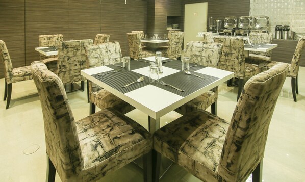A dining area with a square table surrounded by upholstered chairs with a marbled pattern.