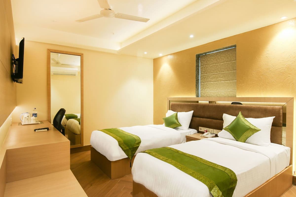 Habitación de hotel con dos camas, un escritorio, un espejo y un ventilador de techo.