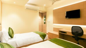 A hotel room with two beds, a desk, a chair, a flat-screen TV, and an air conditioning unit. - Treebo Hoops - Airport, VIP Road (Barasat)