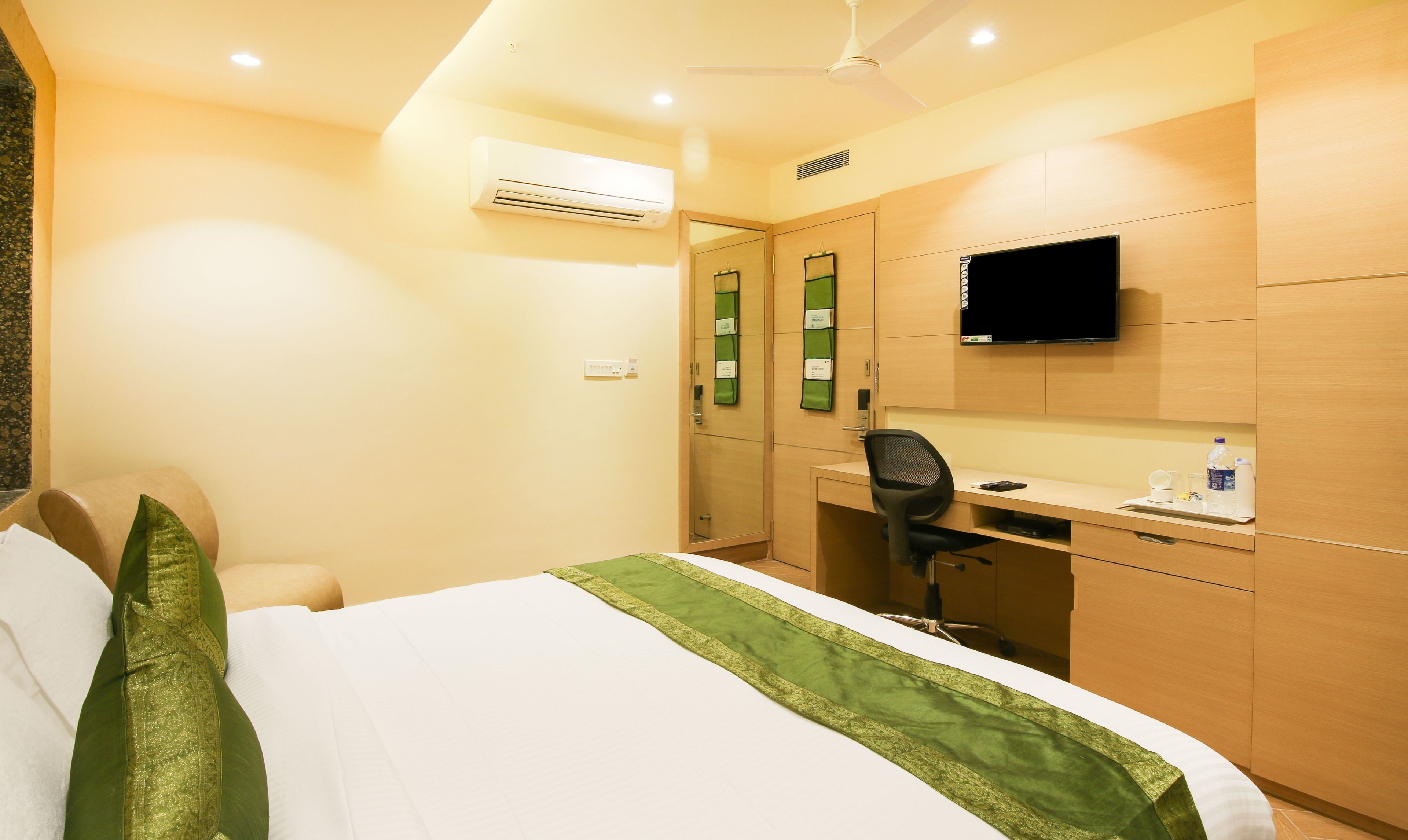 Habitación de hotel con cama, escritorio, silla, aire acondicionado, televisión y espejo.