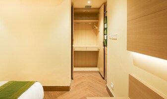 Un pasillo estrecho con un armario de madera, una pequeña estantería y una cama con colcha verde.