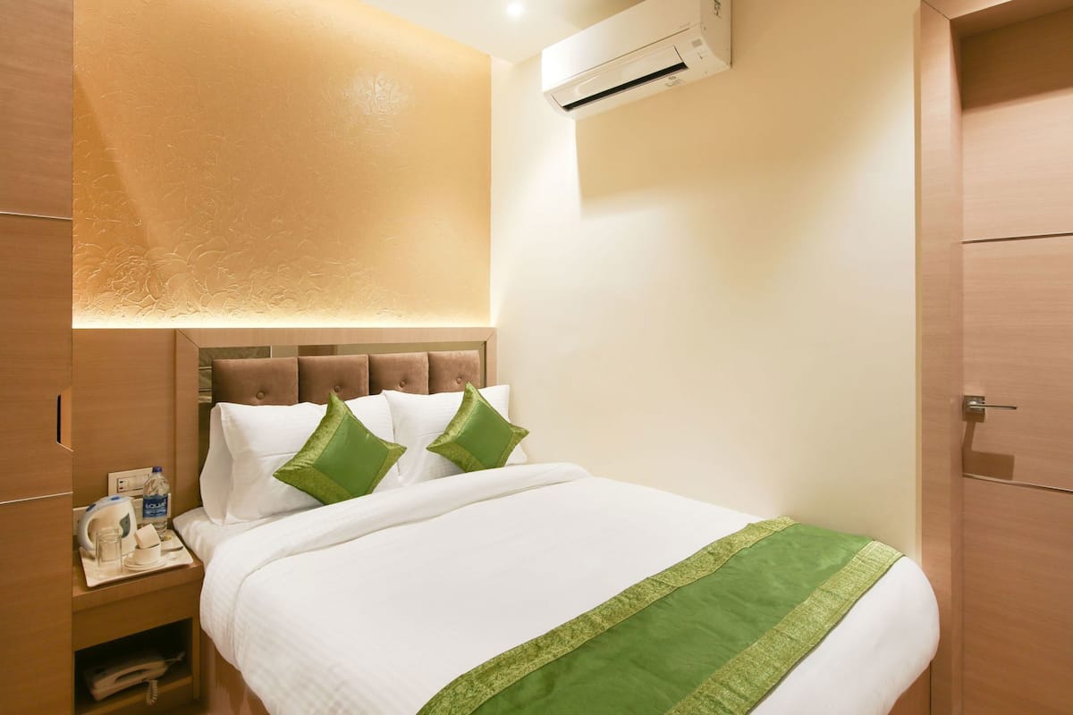 Una habitación de hotel con cama, mesita de noche, aire acondicionado y armario.