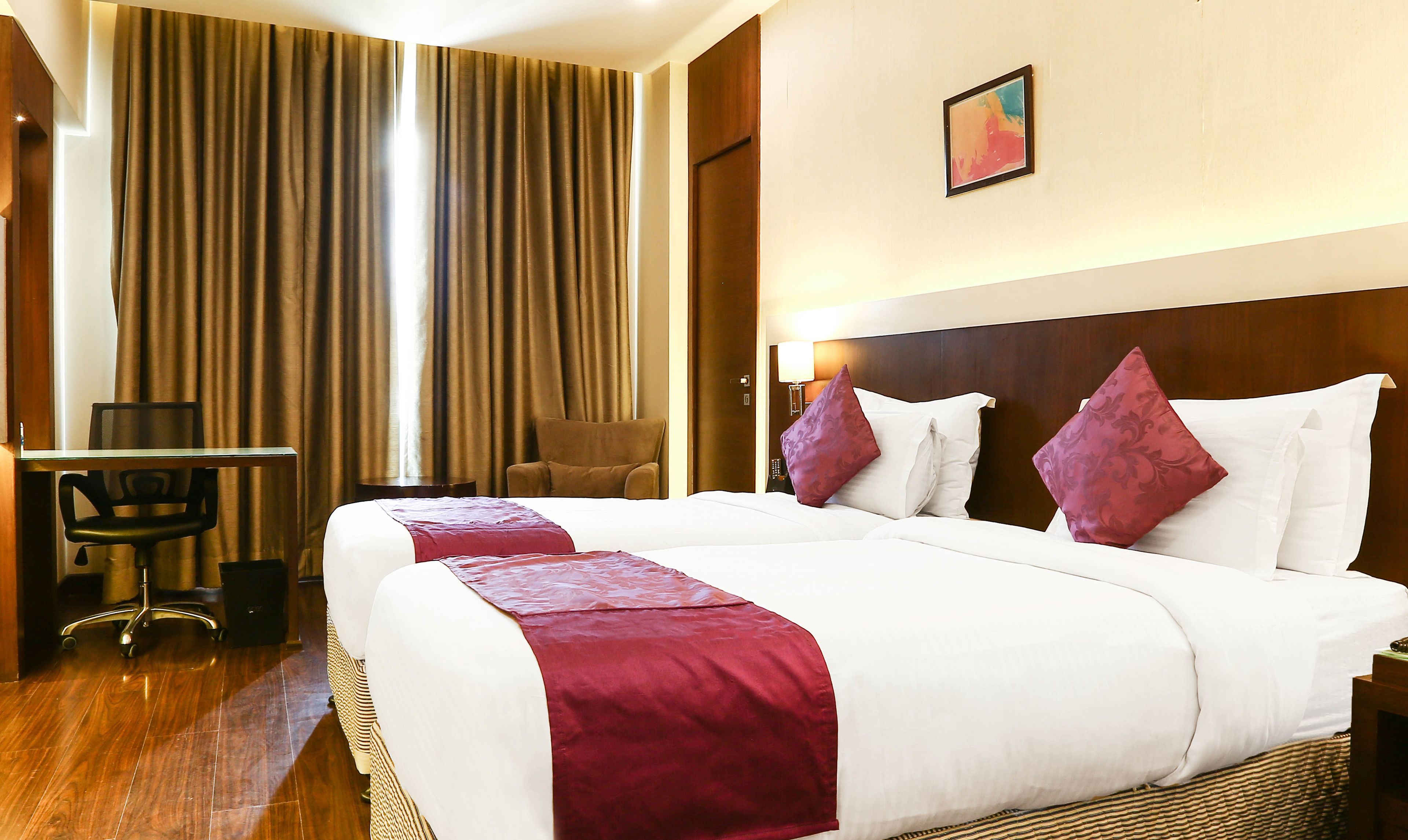 A hotel room with a large bed, a desk, a chair, and a painting on the wall.