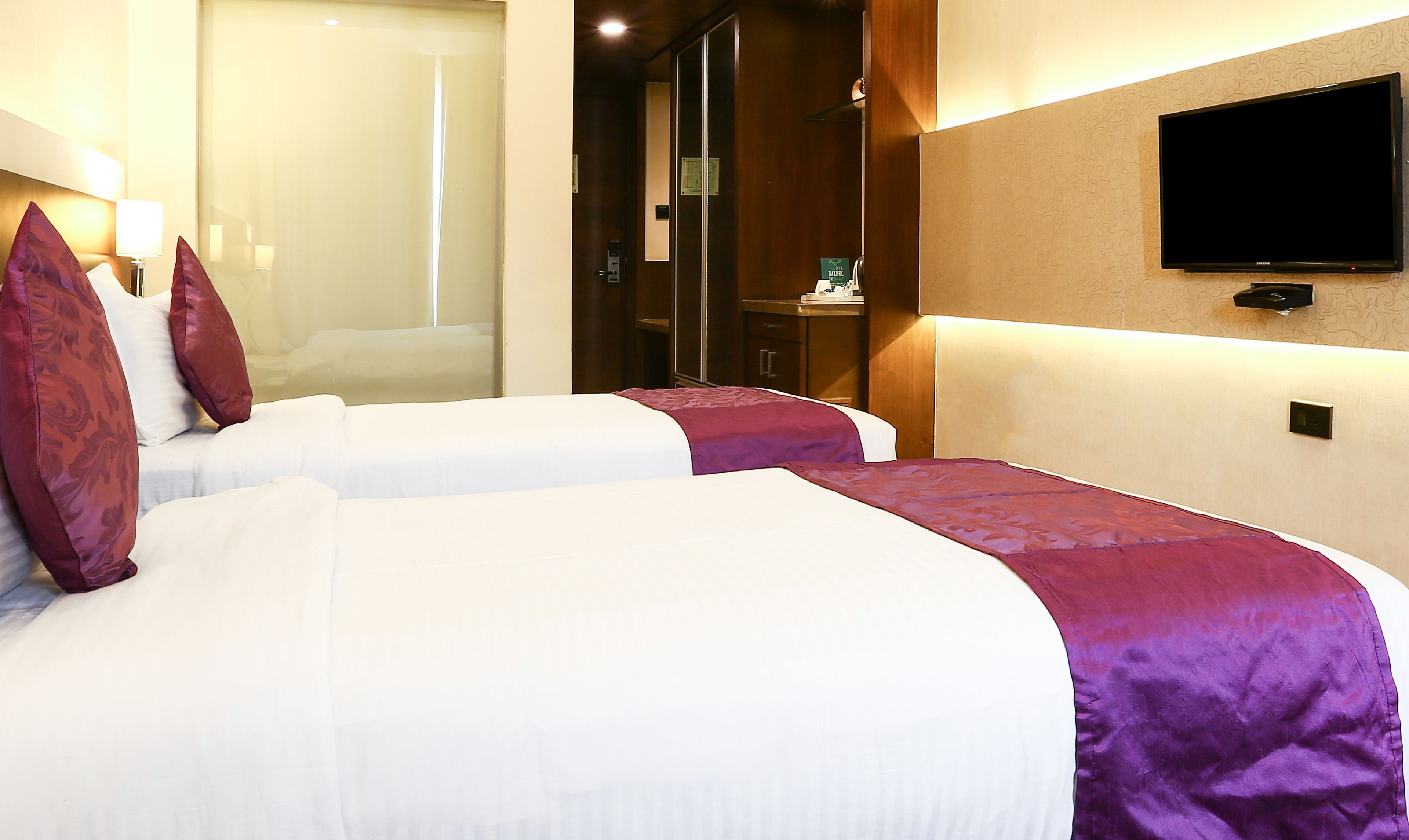 Een hotelkamer met twee bedden, een aan de muur bevestigde televisie en een spiegel.