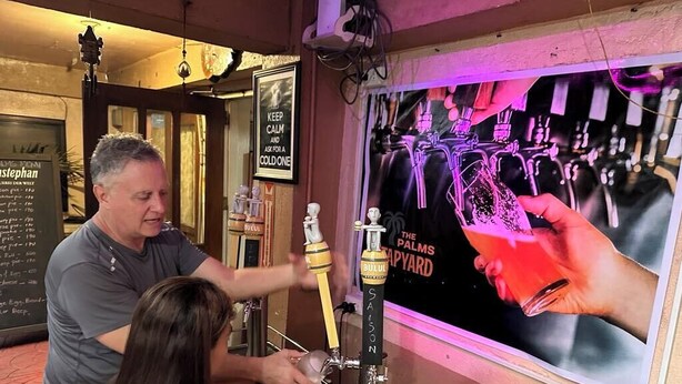 A bar area with a tap labeled 'The Palms' and a poster of hands holding a glass. - 1st Street Park Apartelle (Angeles City)