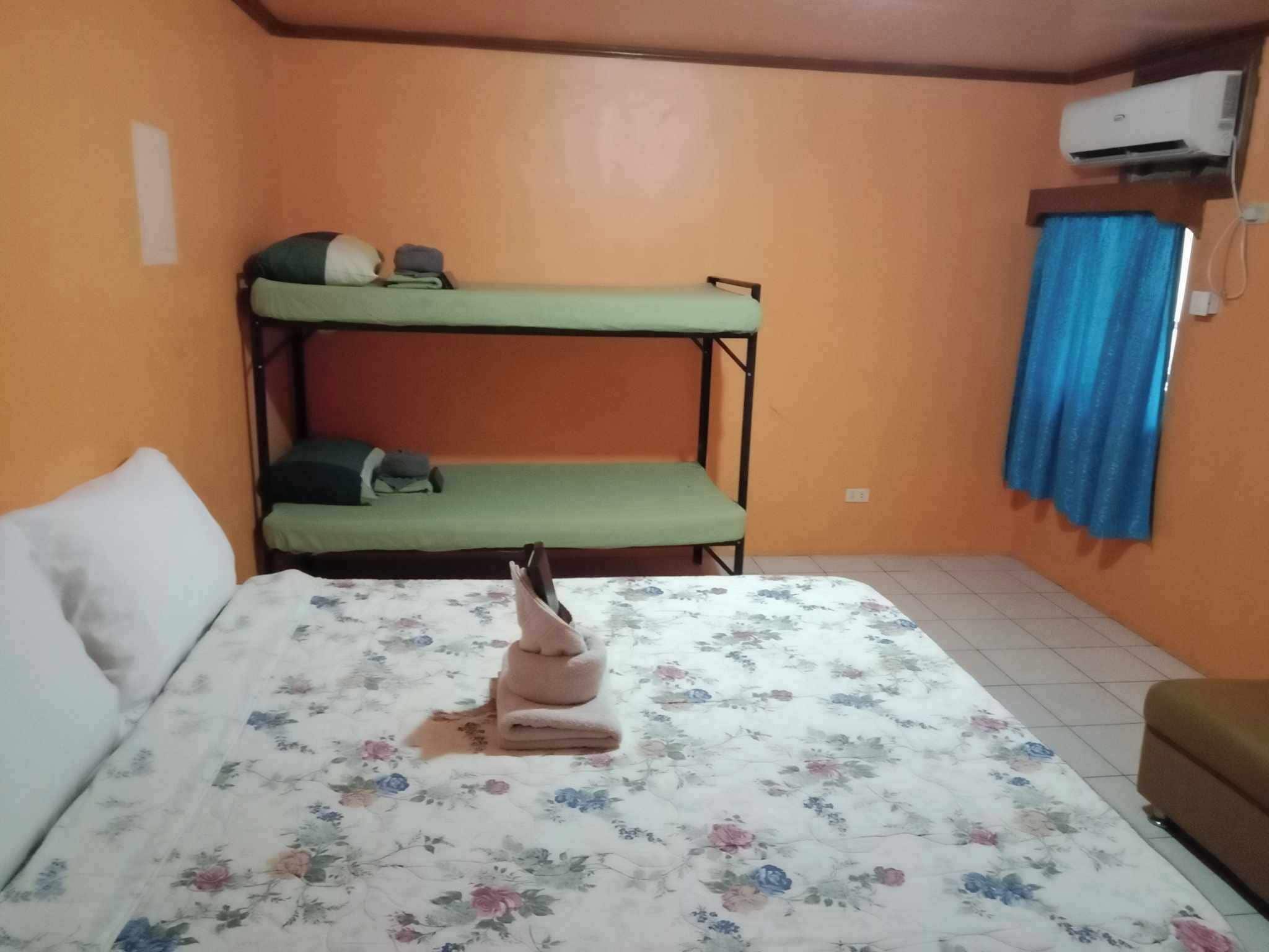 A room with a bunk bed, a single bed with floral bedding, a brown sofa, and an air conditioning unit.